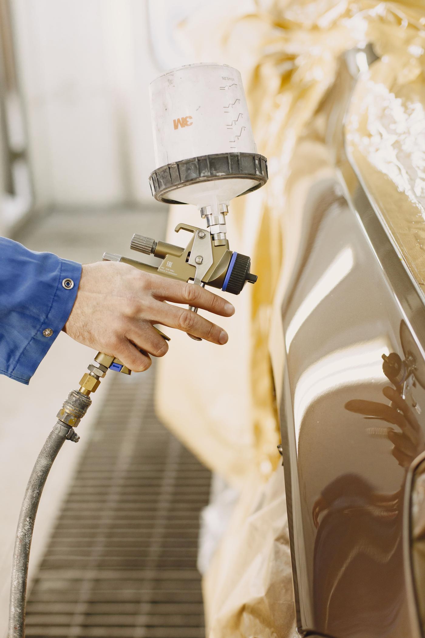 A technician in protective suit spray painting a car bumper